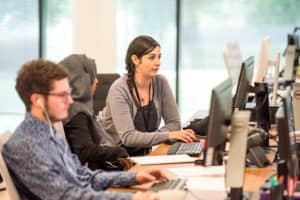 Female manager showing new employee how to use the IT system in relaxed office setting during recruitment onboarding process.