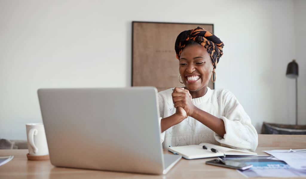 Shot of a young woman cheering while working on a laptop at home