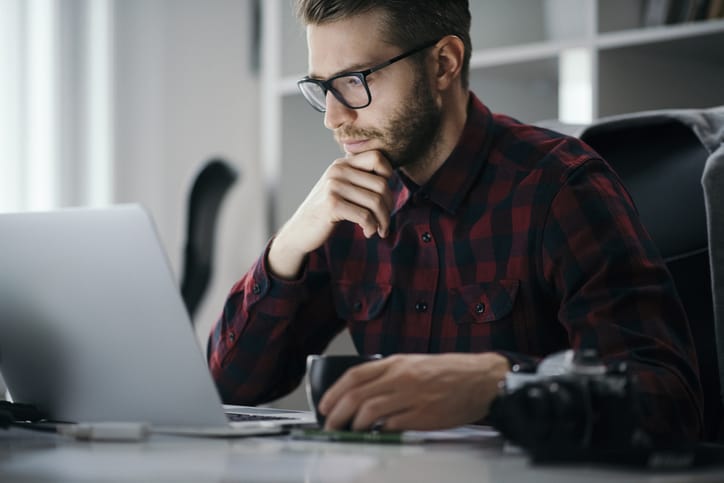 Young man drinking coffee while working on a laptop at office